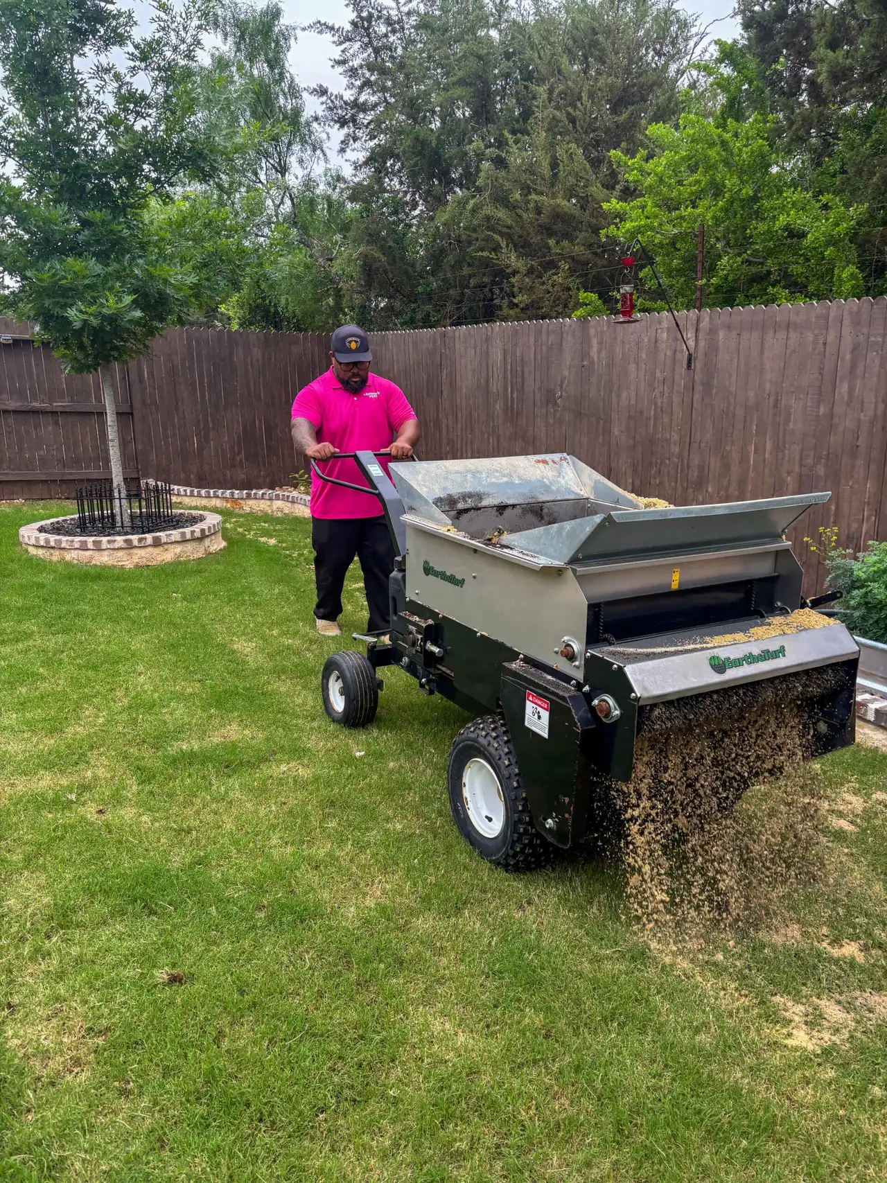 Lawn technician spreading compost top dressing with EarthAndTurf topdresser in fenced backyard