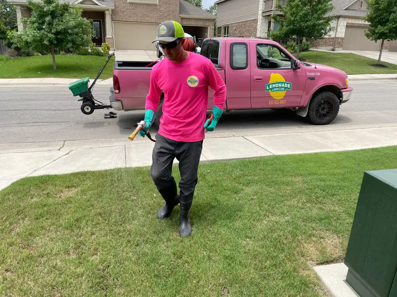 Lawn care technician spraying treatment on front yard beside pink Lemonade Lawn Care truck