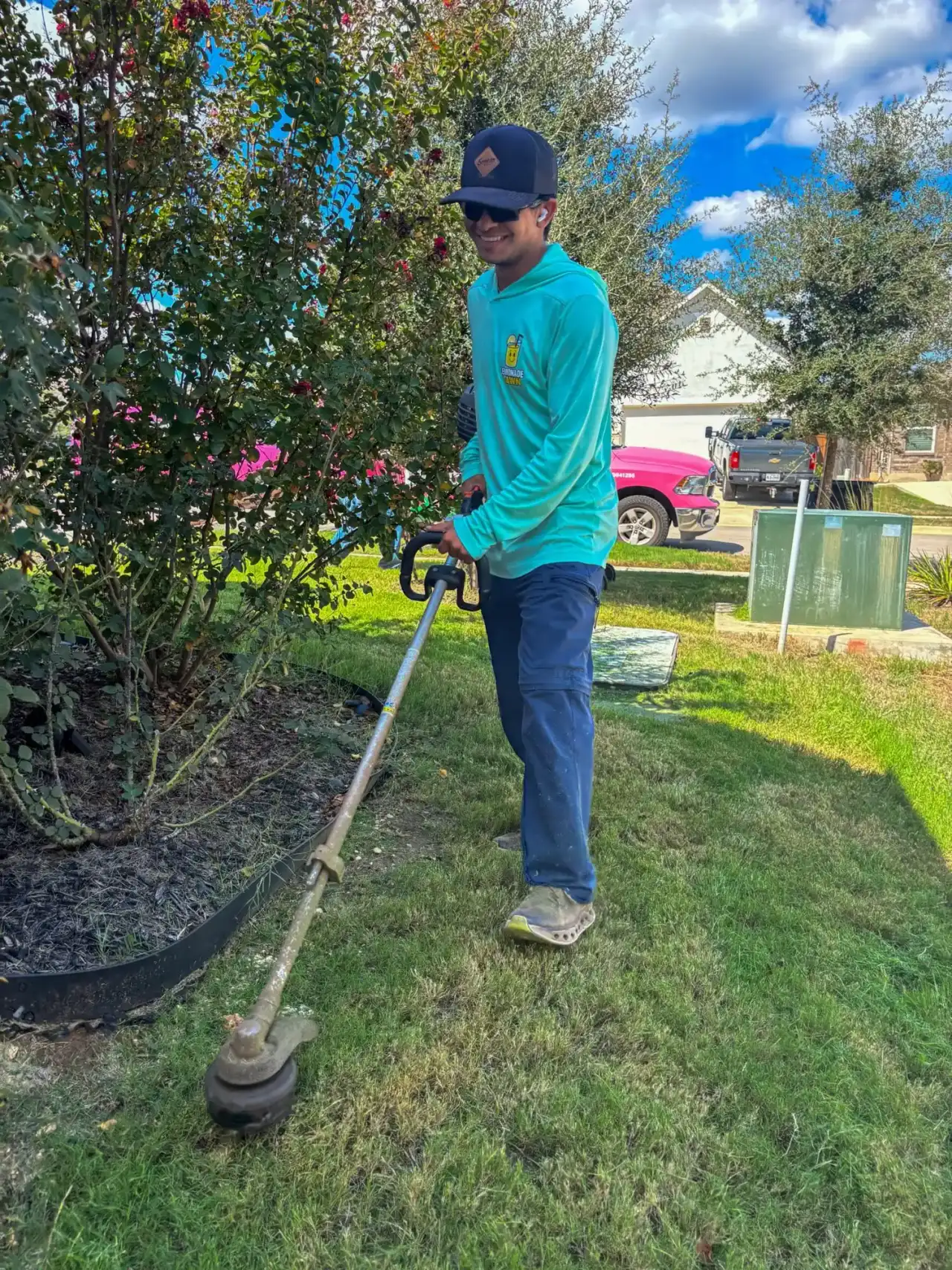 Lemonade Lawn Care technician trimming around a landscape bed in New Braunfels, pink truck behind